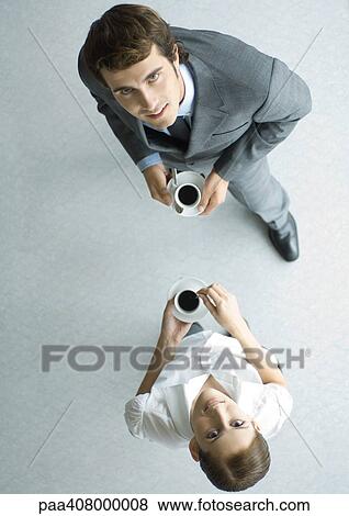 Business associates holding cups of coffee, looking up at camera, full length, high angle view View Large Photo Image Stock Photo - Business associates holding cups of coffee, looking up at camera, full length, high angle view. Fotosearch