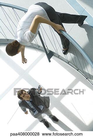 Businessman holding cell phone up to woman from lower floor, full length, high angle view View Large Photo Image Stock Photo - Businessman holding cell phone up to woman from lower floor, full length, high angle view. Fotosearch