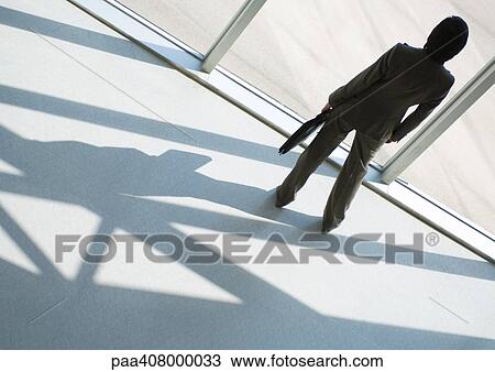 Stock Image - Businesswoman looking out of window, full length, high angle rear view. Fotosearch