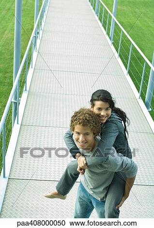 Teenage boy carrying teenage girl piggyback on walkway View Large Photo Image Stock Image - Teenage boy carrying teenage girl piggyback on walkway. Fotosearch
