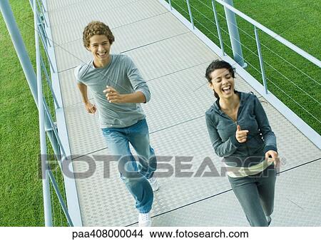 Picture - Teenage couple running on walkway, laughing, high angle view. Fotosearch