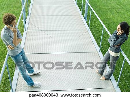 Teenage couple standing face to face on walkway, using cell phones, full length, high angle view View Large Photo Image Stock Image - Teenage couple standing face to face on walkway, using cell phones, full length, high angle view. Fotosearch