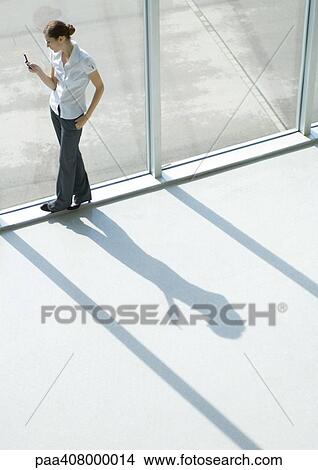 Woman using cell phone by window, full length, high angle view View Large Photo Image Picture - Woman using cell phone by window, full length, high angle view. Fotosearch