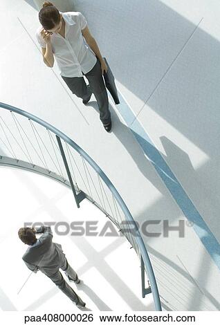Woman using cell phone near railing, on lower floor, businessman walking by using cell phone, high angle view View Large Photo Image Stock Photograph - Woman using cell phone near railing, on lower floor, businessman walking by using cell phone, high angle view. Fotosearch