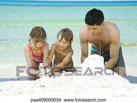 Father and two children playing in sand on beach View Large Photo Image Picture - Father and two children playing in sand on beach. Fotosearch