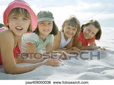 Stock Photograph - Four girls lying on beach, smiling at camera, close-up. Fotosearch