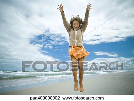 Stock Image - Girl jumping on beach, full length. Fotosearch