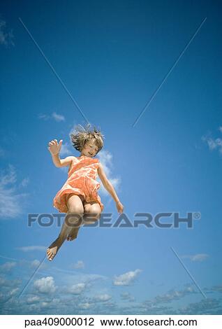 Stock Image - Girl jumping, sky in background, low angle view. Fotosearch