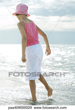 Stock Photo - Girl standing in surf at beach, rear view. Fotosearch