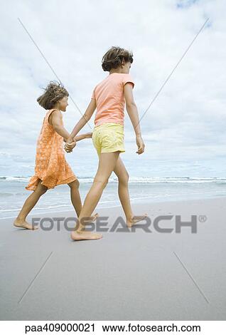 Stock Image - Two girls walking, holding hands, on beach. Fotosearch