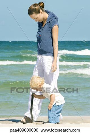 Stock Photograph - Young woman walking on beach next to toddler. Fotosearch