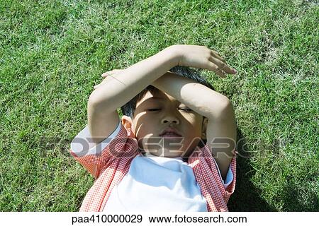 Boy lying on grass, holding arms over face View Large Photo Image Stock Photo - Boy lying on grass, holding arms over face. Fotosearch