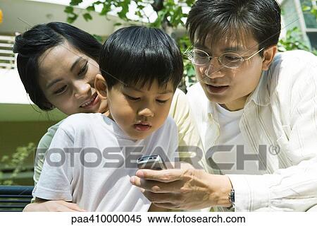 Boy with mother and father, father holding out cell phone for boy to see View Large Photo Image Stock Photography - Boy with mother and father, father holding out cell phone for boy to see. Fotosearch