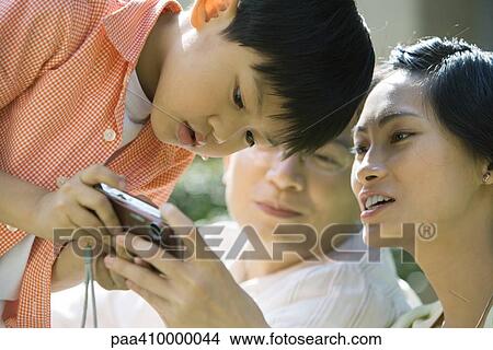 Boy with parents, mother holding digital camera, boy bending over to look View Large Photo Image Picture - Boy with parents, mother holding digital camera, boy bending over to look. Fotosearch