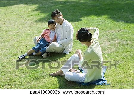 Family sitting on grass, woman taking photo of man and boy View Large Photo Image Stock Photography - Family sitting on grass, woman taking photo of man and boy. Fotosearch