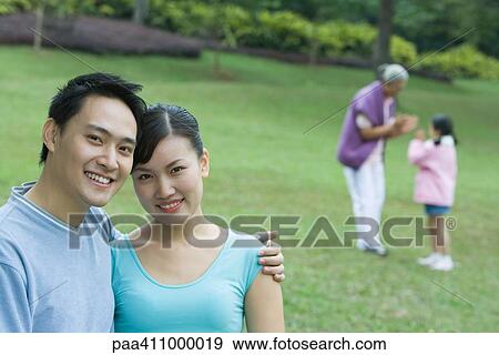 Couple smiling at camera, senior woman and girl in background View Large Photo Image Stock Photo - Couple smiling at camera, senior woman and girl in background. Fotosearch