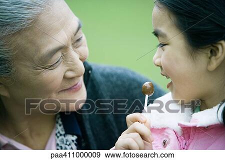 Stock Photo - Girl eating lollipop, looking at grandmother, close-up. Fotosearch