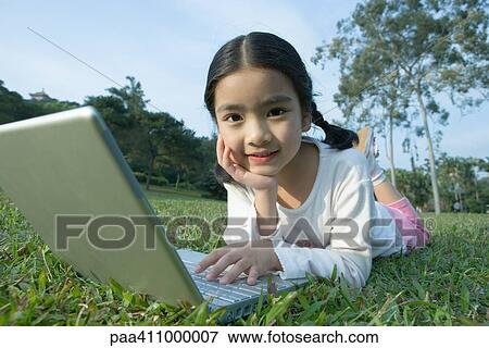 Girl lying on grass using laptop View Large Photo Image Stock Photo - Girl lying on grass using laptop. Fotosearch