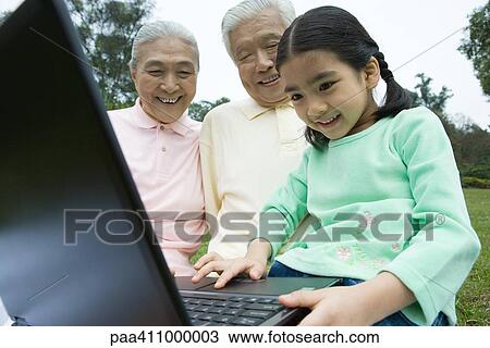 Stock Image - Girl using laptop while grandparents watch. Fotosearch