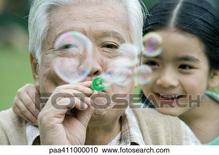 Senior man blowing bubbles, girl leaning on shoulder, close-up View Large Photo Image Stock Image - Senior man blowing bubbles, girl leaning on shoulder, close-up. Fotosearch