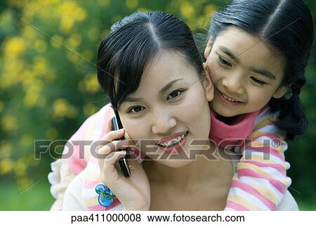 Woman using cell phone while girl leans over shoulder View Large Photo Image Stock Photo - Woman using cell phone while girl leans over shoulder. Fotosearch
