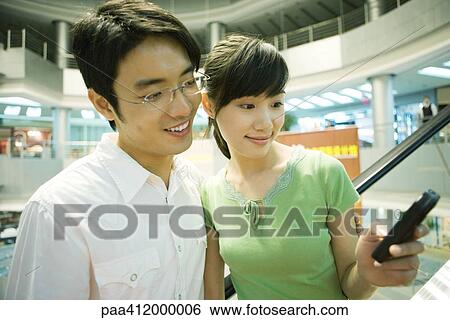 Stock Photograph - Couple looking at cell phone in mall. Fotosearch