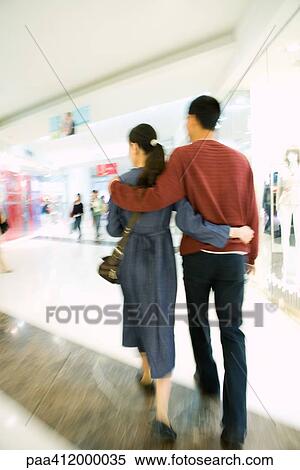 Stock Photography - Couple walking through shopping mall, rear view, full length. Fotosearch