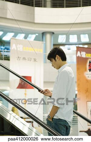 Man on escalator checking cell phone View Large Photo Image Stock Photograph - Man on escalator checking cell phone. Fotosearch