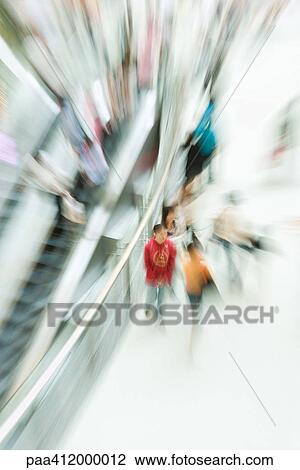 Stock Image - People walking in public space next to escalator, blurred motion. Fotosearch