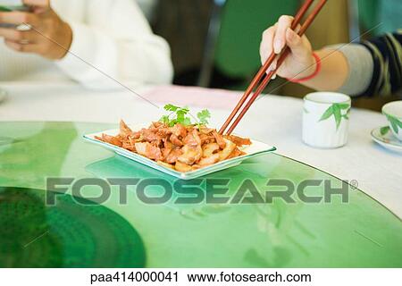 Couple sitting at table, having meal, woman eating from dish with chopsticks, partial view View Large Photo Image Stock Image - Couple sitting at table, having meal, woman eating from dish with chopsticks, partial view. Fotosearch