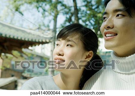 Picture - Couple standing side by side, looking out of frame, traditional Chinese building in background. Fotosearch