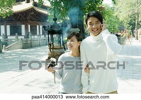 Couple walking near temple, man using cell phone and woman holding camera View Large Photo Image Stock Image - Couple walking near temple, man using cell phone and woman holding camera. Fotosearch