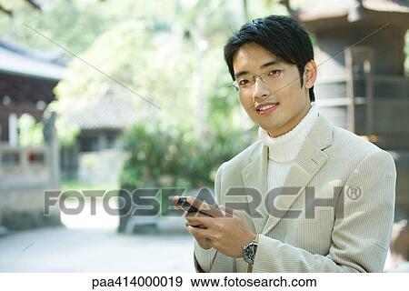Man holding cell phone, smiling at camera View Large Photo Image Stock Photo - Man holding cell phone, smiling at camera. Fotosearch