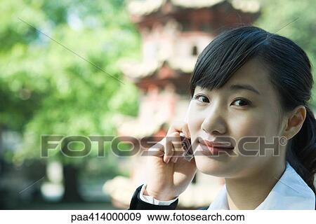 Woman using cell phone, pagoda in background, close-up View Large Photo Image Stock Photo - Woman using cell phone, pagoda in background, close-up. Fotosearch