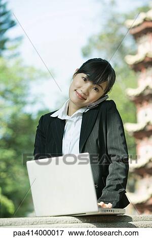 Woman using laptop and cell phone, pagoda in background View Large Photo Image Stock Photo - Woman using laptop and cell phone, pagoda in background. Fotosearch