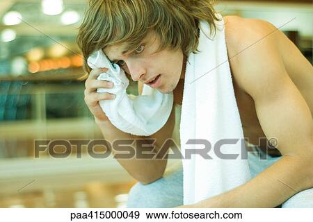 Stock Photo - Barechested man with towel around neck, leaning forward and wiping forehead. Fotosearch