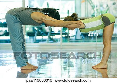 Stock Photography - Two young adults bending forward at waist, grasping each other's shoulders, side view. Fotosearch