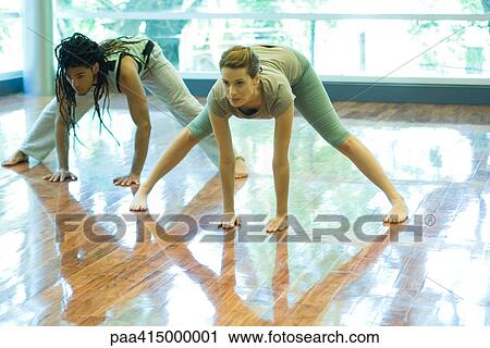 Stock Image - Two young adults doing prasarita padottanasana pose in yoga class. Fotosearch