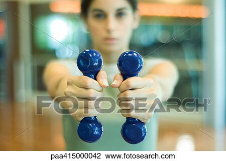 Stock Image - Woman holding out dumbbells. Fotosearch