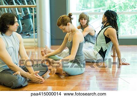 Picture - Young adults sitting on gym floor chatting before exercise class. Fotosearch