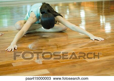 Stock Image - Young woman doing seating forward bend during exercise class. Fotosearch