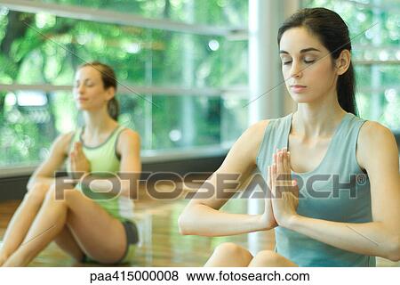 Stock Photo - Young women sitting with eyes closed and hands in prayer position during yoga class. Fotosearch