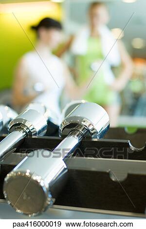Dumbbells on rack, women in blurred background View Large Photo Image Stock Photo - Dumbbells on rack, women in blurred background. Fotosearch
