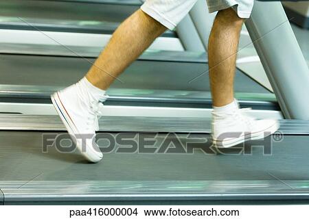 Picture - Man running on treadmill, knee down, blurred motion. Fotosearch
