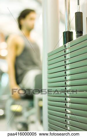 Stock Photography - Man working out with weight machine, focus on weights in foreground. Fotosearch