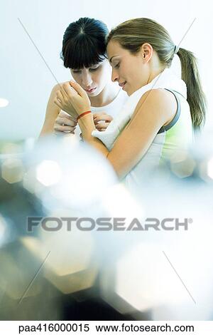 Stock Photography - Woman helping second woman in exercise clothes remove bracelet. Fotosearch