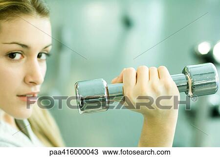 Stock Image - Woman holding up dumbbell, partial view. Fotosearch