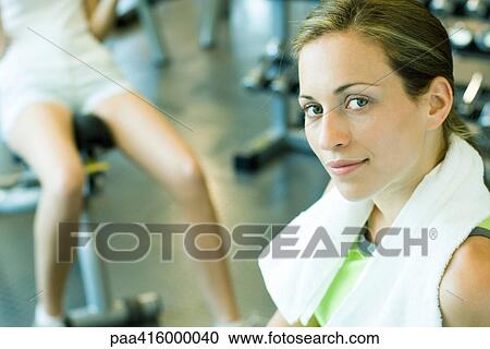 Stock Image - Woman in health club with towel around neck, smiling at camera. Fotosearch