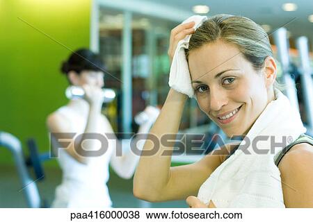Woman in weight room, wiping forehead, smiling at camera View Large Photo Image Stock Photo - Woman in weight room, wiping forehead, smiling at camera. Fotosearch