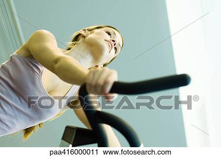 Stock Image - Woman riding exercise bike. Fotosearch
